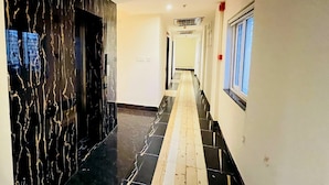 Un couloir avec un mur de marbre sur le côté gauche et une fenêtre sur le côté droit.