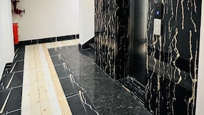 Un couloir moderne avec un sol et des murs en marbre noir, un ascenseur et un extincteur sur le côté gauche.