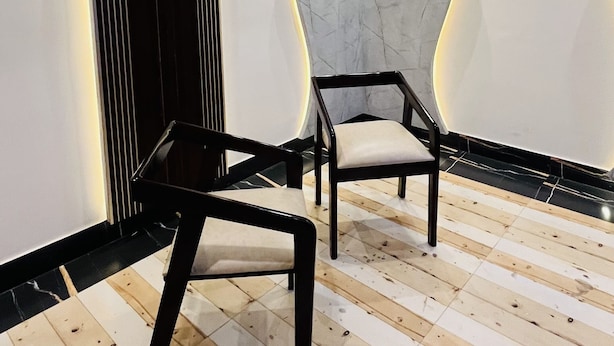 Une pièce moderne avec un plancher en bois, deux chaises noires, un ventilateur de plafond et un mur orné d’un motif ondulé.