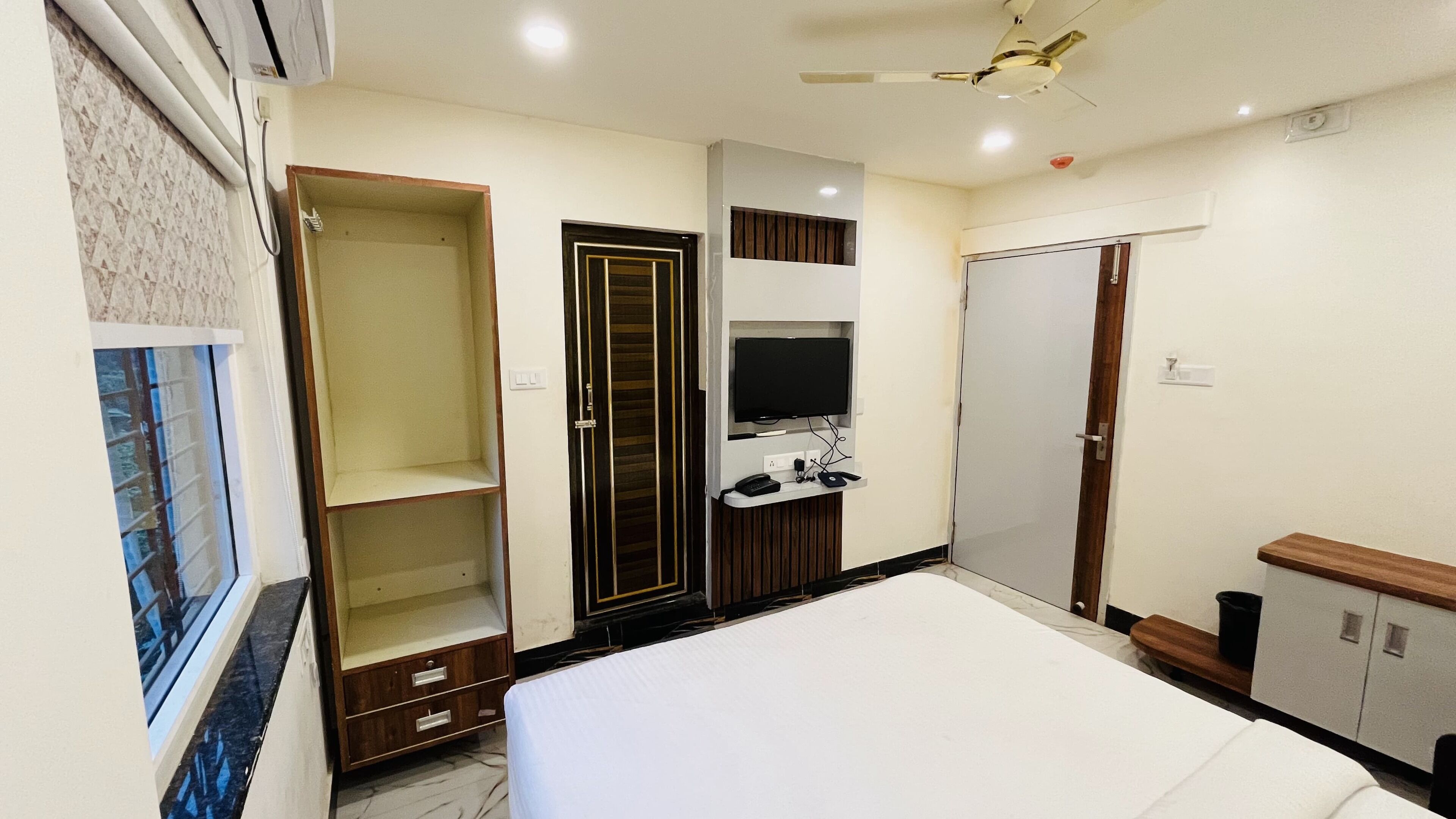 A bedroom with a bed, a wardrobe, a TV mounted on the wall, and a ceiling fan.