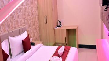 Habitación de hotel con cama, armario de madera, escritorio pequeño con tetera y alfombra roja.