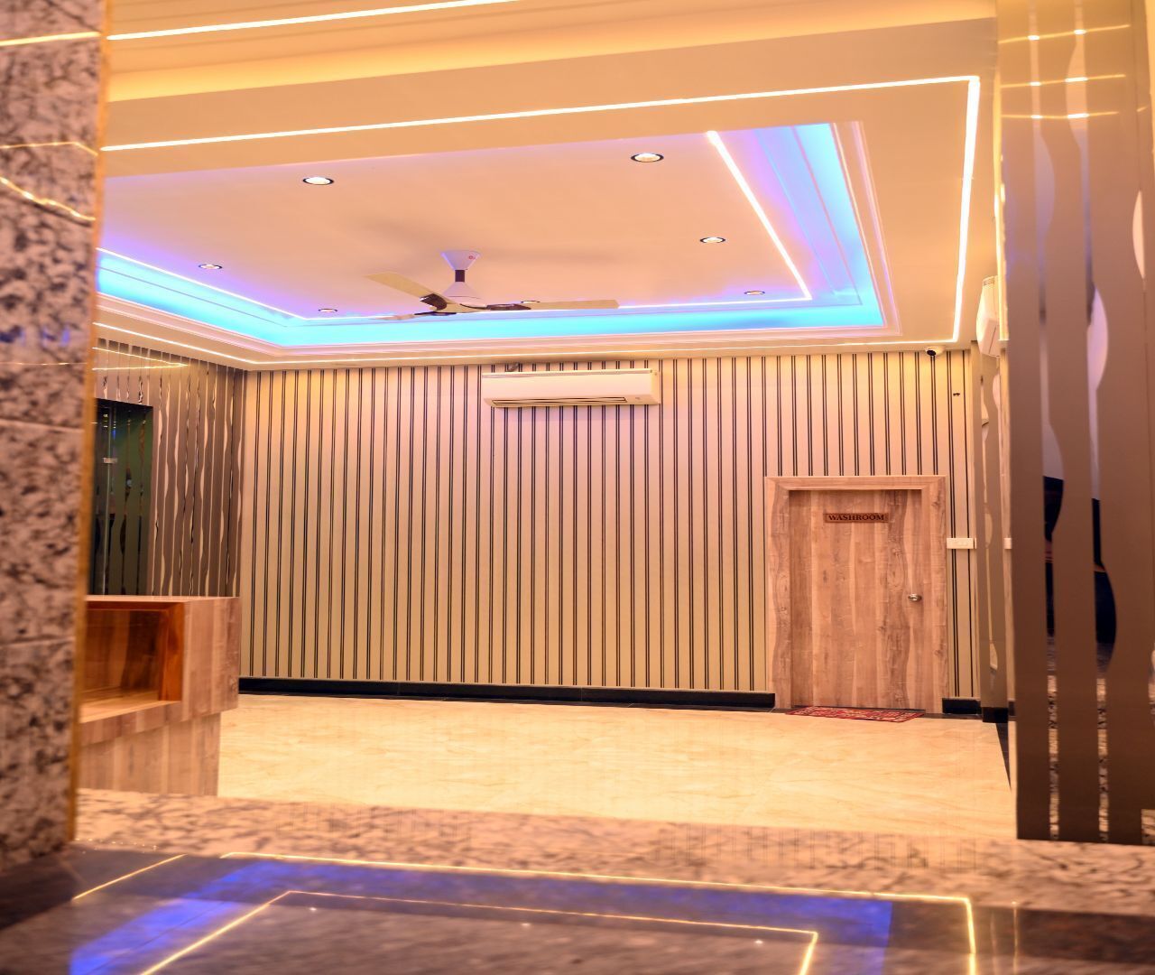 A modern interior with a wooden panel wall, a ceiling fan, recessed lighting, and a wooden door labeled "WASHROOM".