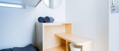 Una habitación minimalista con una cama, un estante de madera y un espejo.
