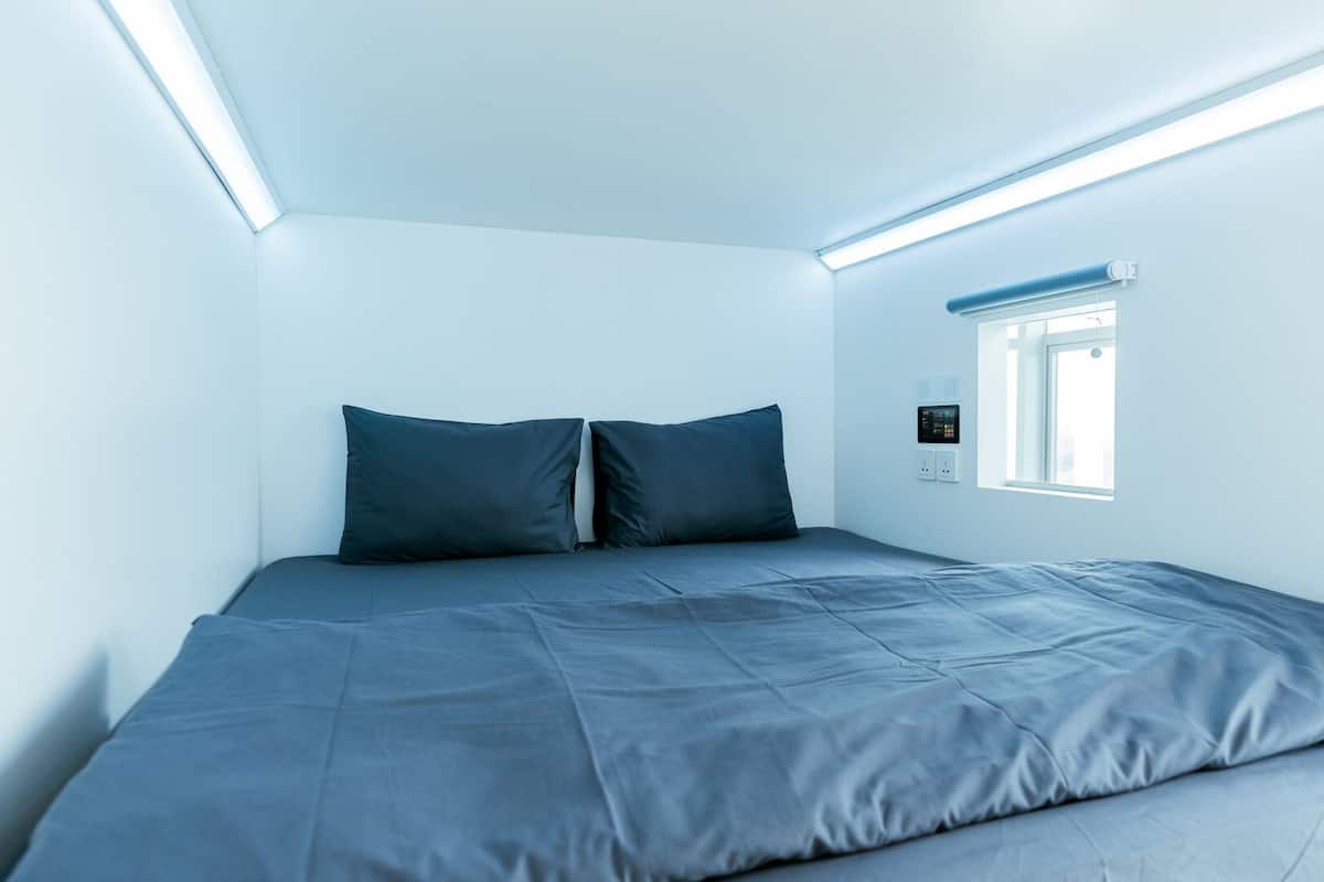 Un dormitorio minimalista con una cama individual, una ventana y un panel de control en la pared.