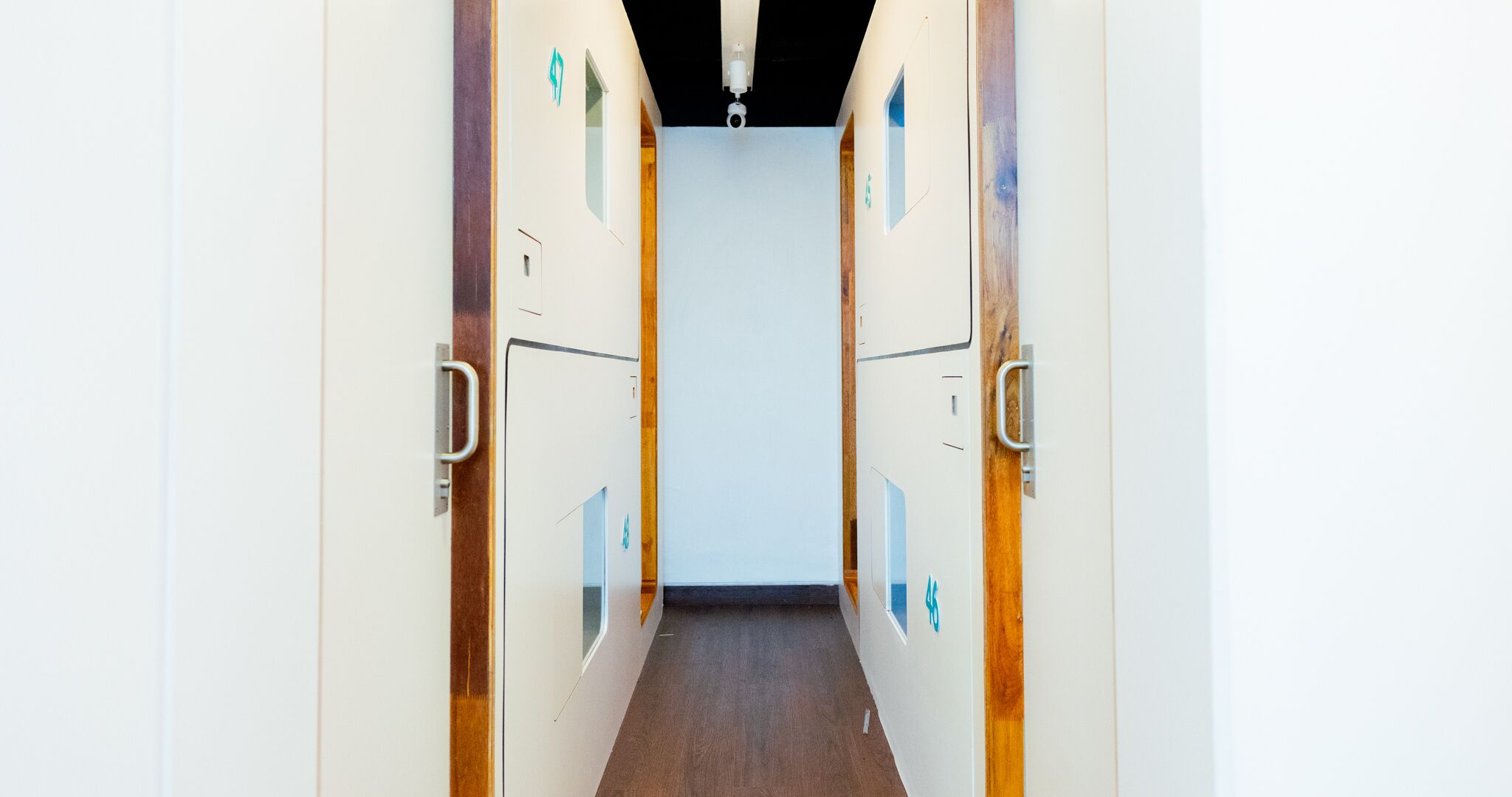 A corridor with lockers on both sides, leading to a room with a white ceiling and a security camera.