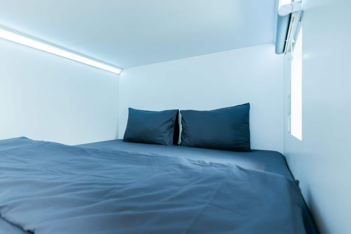Un dormitorio pequeño y moderno con una cama individual, una lámpara en el techo y una ventana.