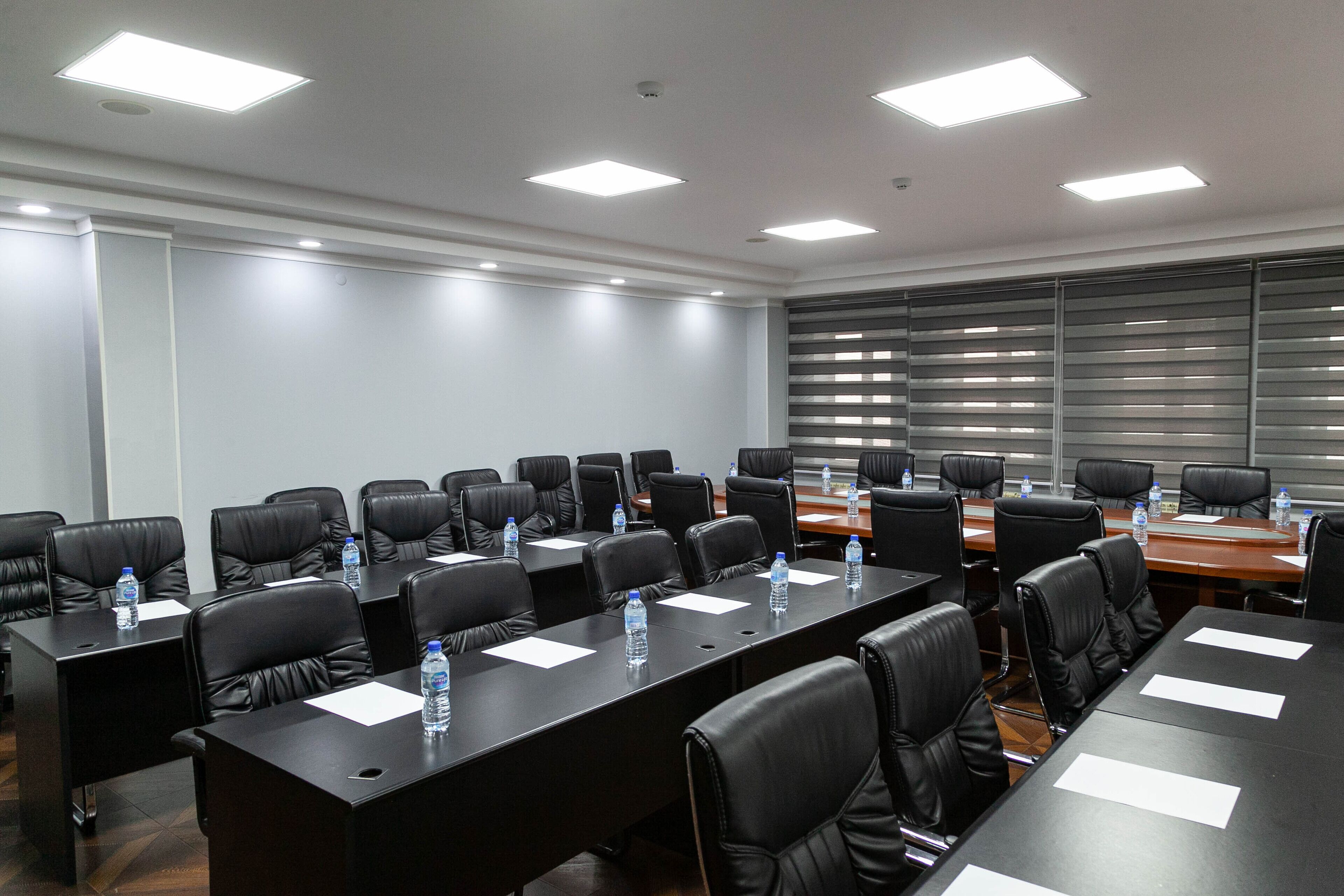 A conference room with multiple tables, black leather chairs, and water bottles on each table.