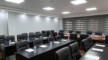 A conference room with multiple tables, black leather chairs, and water bottles on each table.
