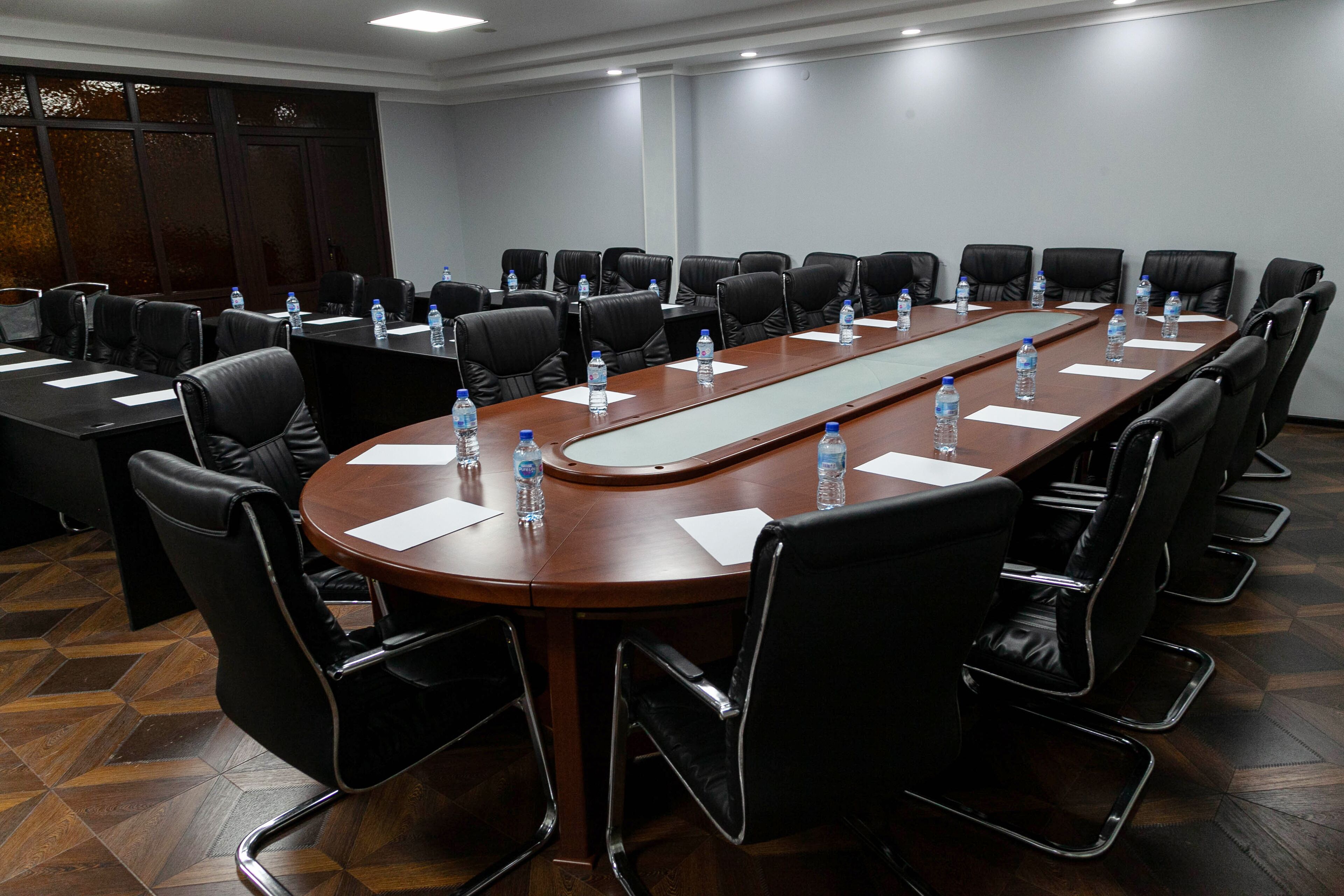 A conference room with a long table, black leather chairs, water bottles, and white notepads.