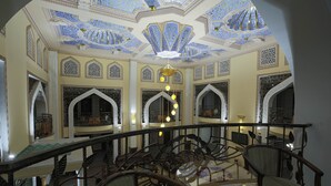 A grand interior with ornate ceilings, a central chandelier, and a balcony with a railing.
