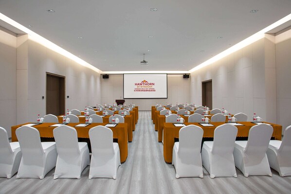 A conference room with multiple tables and chairs, a projector screen, and a podium. - Hawthorn by Wyndham Honghe Mile Hot Spring (Honghe)