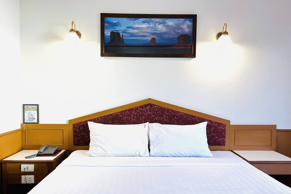 A hotel room with a bed, a nightstand, a telephone, a framed picture on the wall, and two wall-mounted lamps.