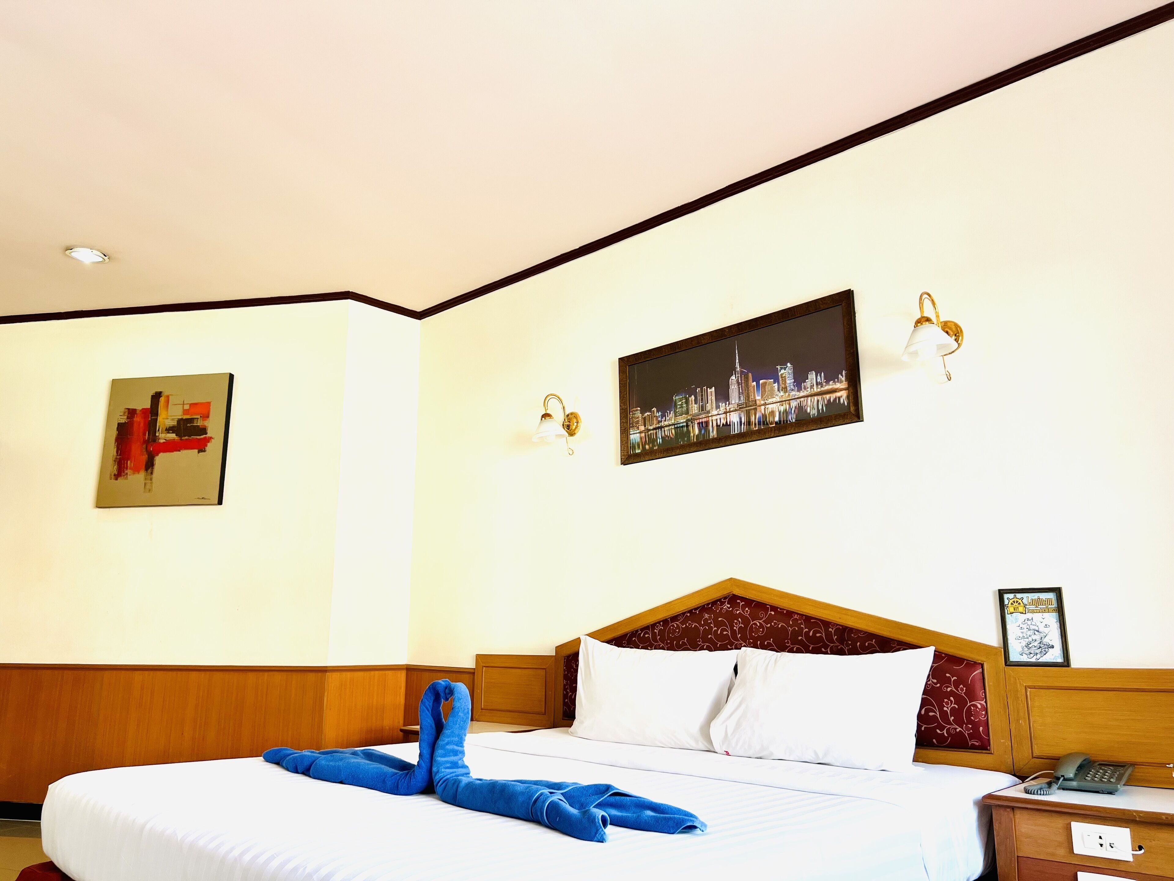 Quarto de hotel com cama bem arrumada, pintura de paisagem urbana e quadro na parede.