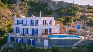 A two-story white building with blue shutters, a swimming pool, and a stone wall.