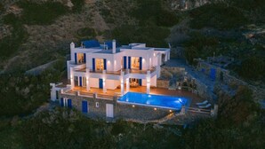 A multi-story modern house with a swimming pool, surrounded by natural landscape.
