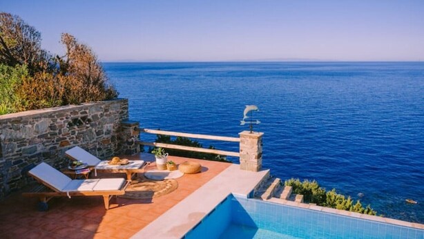 A poolside area with lounge chairs and a stone wall overlooking the sea.
