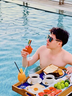 A person in a swimming pool holding a drink, with a tray containing food and beverages. - Sandals Island Hotel  (Nha Trang)