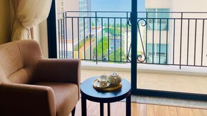 A balcony with a view of the sea and buildings, a sofa, and a small table with a teapot and cups.