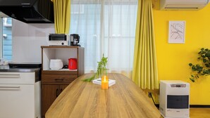 Une cuisine avec une table en bois, un four à micro-ondes, un grille-pain et une bouilloire rouge. Il y a une plante sur la table et un mur jaune en arrière-plan.