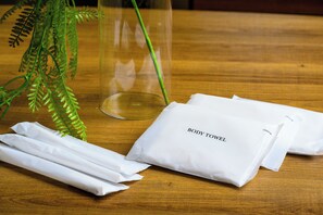 A wooden table with a glass vase, a fern, and white tissue packets labeled "BODY TOWEL".