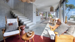 Una sala de estar moderna con una escalera, muebles de madera y ventanas grandes.