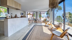 Una sala de estar moderna con un ventanal grande, techo de madera y un comedor con sillas y mesa.