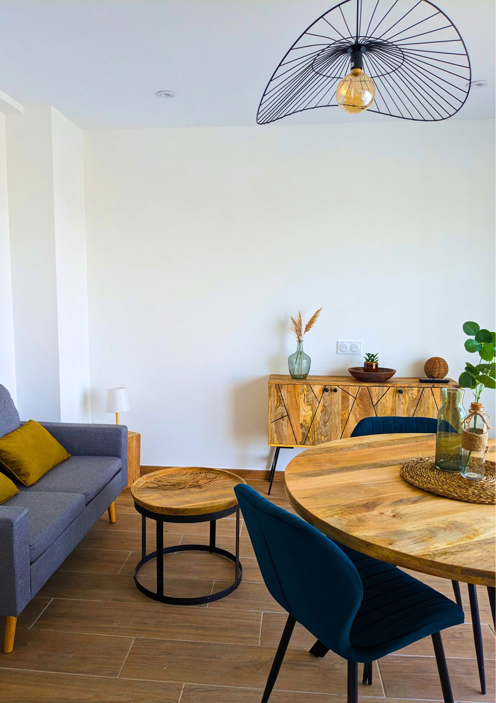 Una sala de estar moderna con un sofá gris, una mesa de comedor redonda de madera y una silla azul.