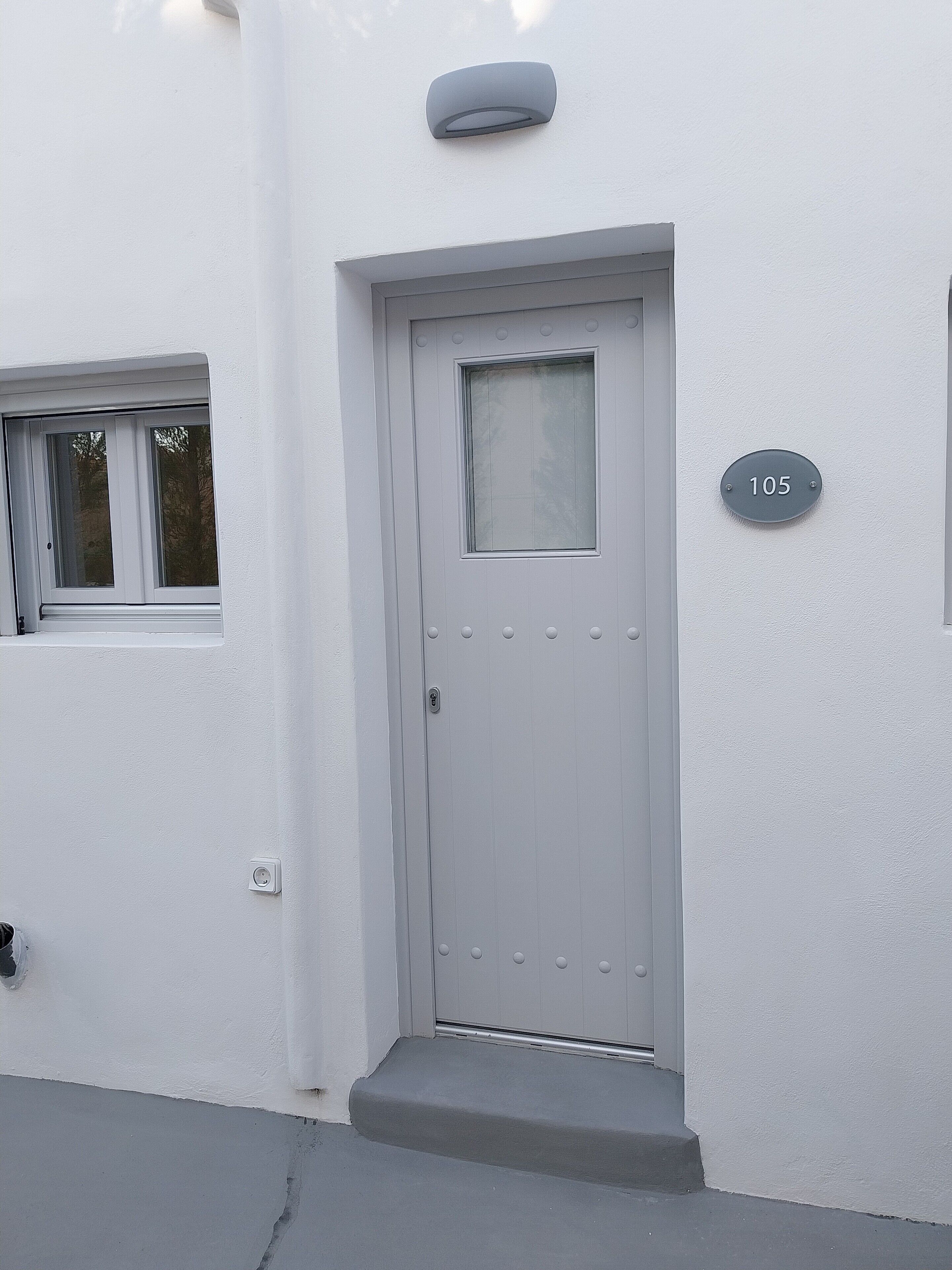 Una puerta blanca con una placa que indica el número '105', una pequeña ventana encima y un timbre sobre la puerta.