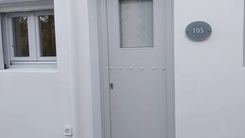 Una puerta blanca con una placa que indica el número '105', una pequeña ventana encima y un timbre sobre la puerta.