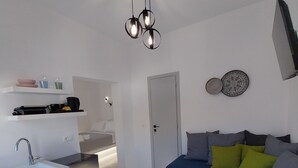 Una habitación moderna y minimalista con cocina integrada, un sofá con cojines y una lámpara de techo original.
