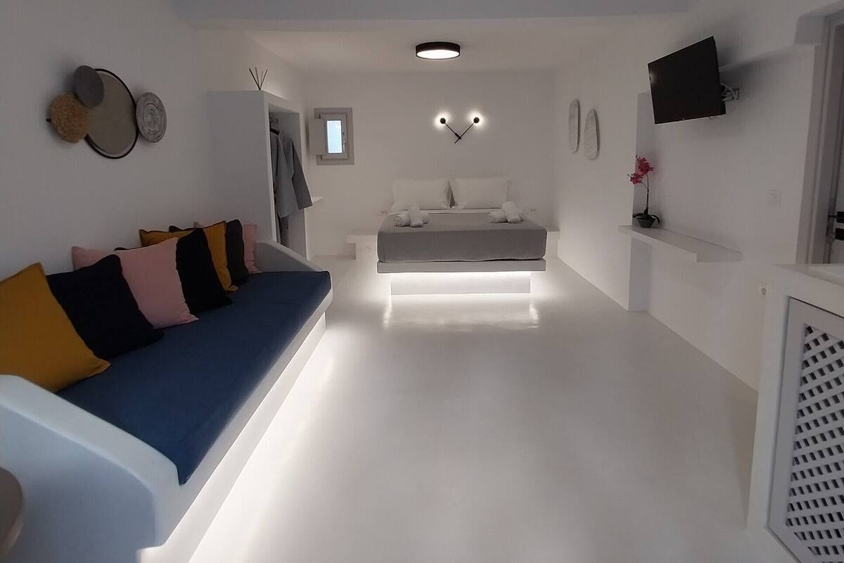Ein moderner, gut beleuchteter Wohnbereich mit einer Couch, einem Bett und einem an der Wand befestigten Fernseher.
