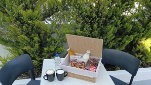 Mesa al aire libre con una cesta de mimbre que contiene alimentos, una botella de agua y dos tazas de café.