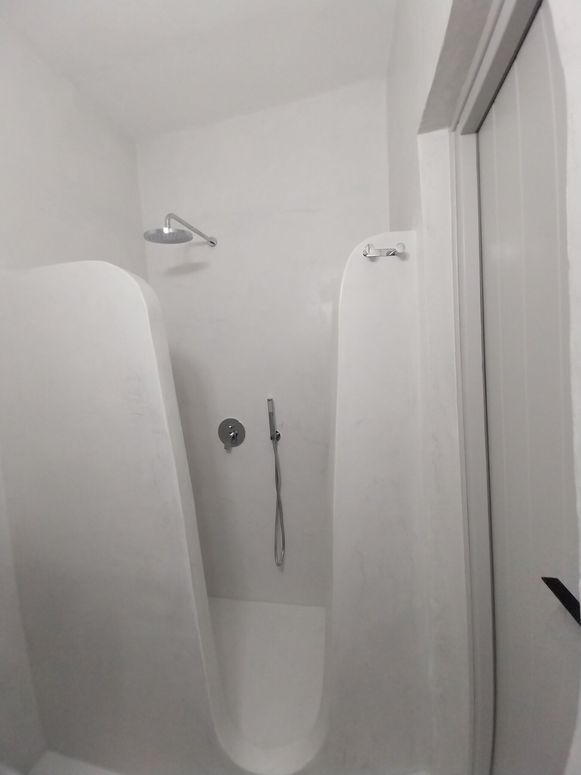 Un área de ducha pequeña y cerrada, con un cabezal de ducha de mano y un grifo empotrado en la pared.