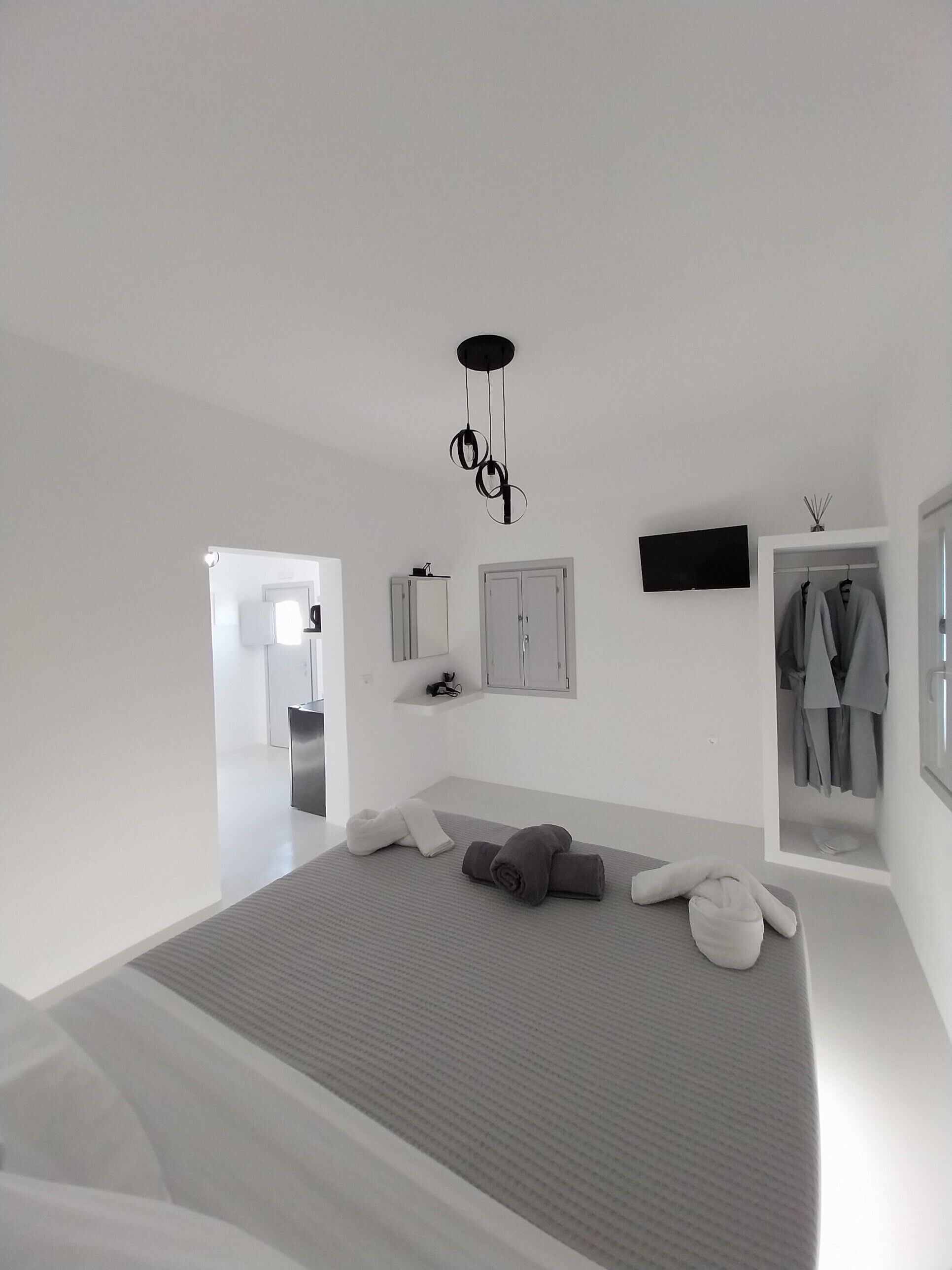 A modern bedroom with a large bed, a TV mounted on the wall, and a wardrobe with hanging clothes.