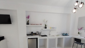 Una cocina moderna con armarios blancos, horno empotrado, lavamanos y comedor con una silla negra.