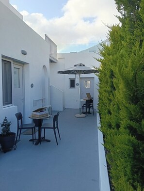 A white building with a covered patio area, a small table with chairs, and a potted plant. - East Wind Perissa (Santorini)