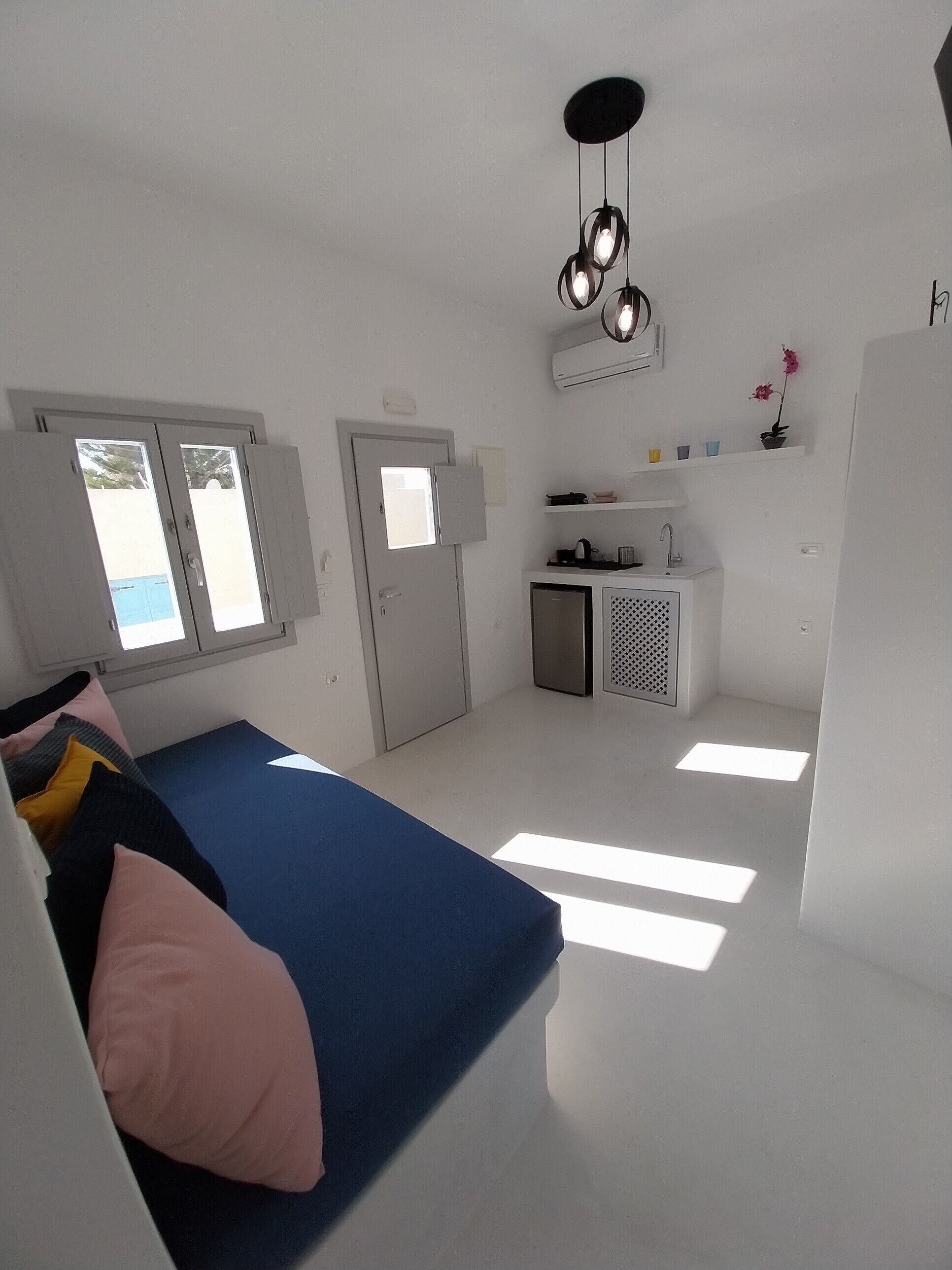 A compact, modern room with a bed, a small kitchenette, and a door leading to an outdoor area.