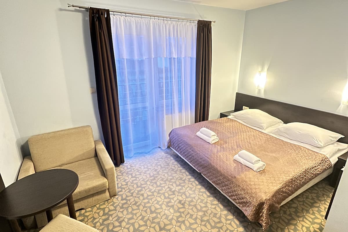 Quarto de hotel com cama, cadeira, mesinha e janela com cortinas.