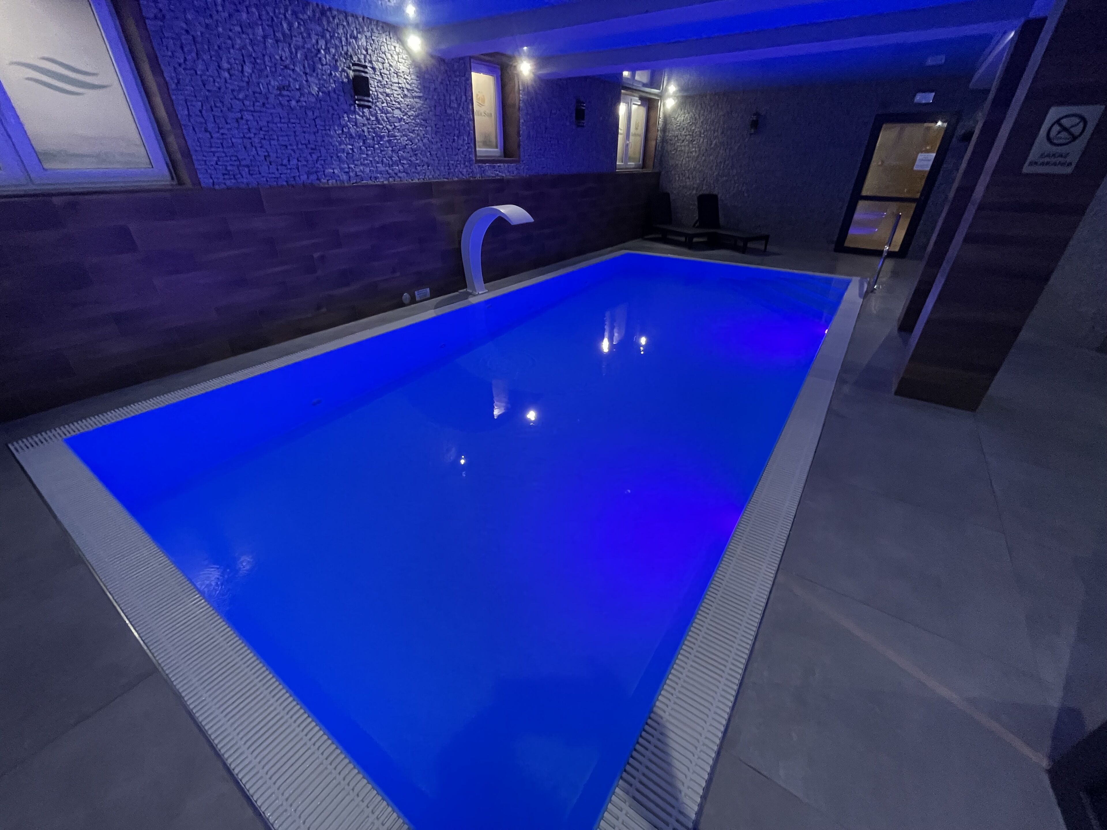 A swimming pool with a blue tint, surrounded by stone walls and a bench.