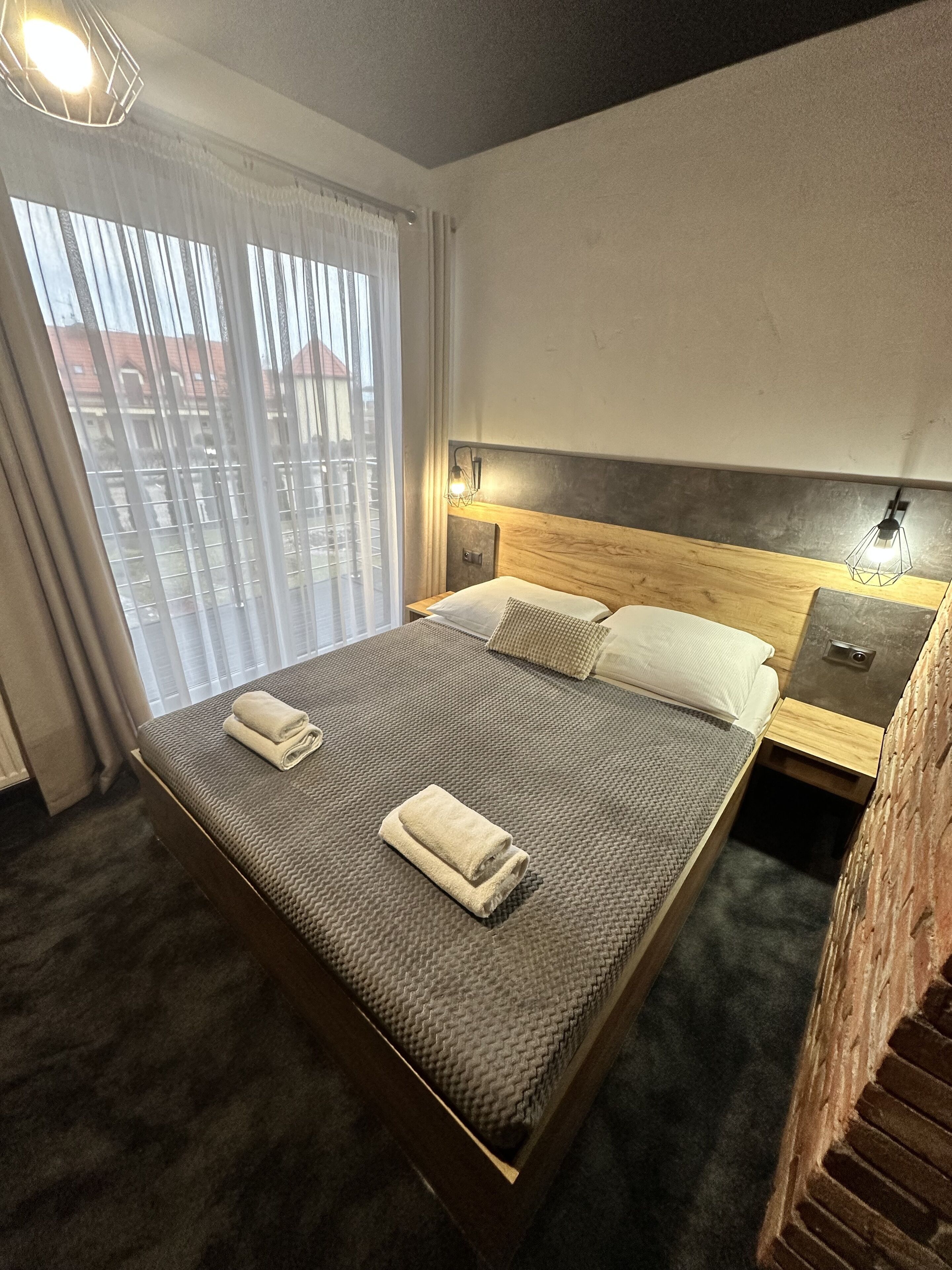 Een hotelkamer met een groot bed, een nachtkastje, een lamp en uitzicht op gebouwen.