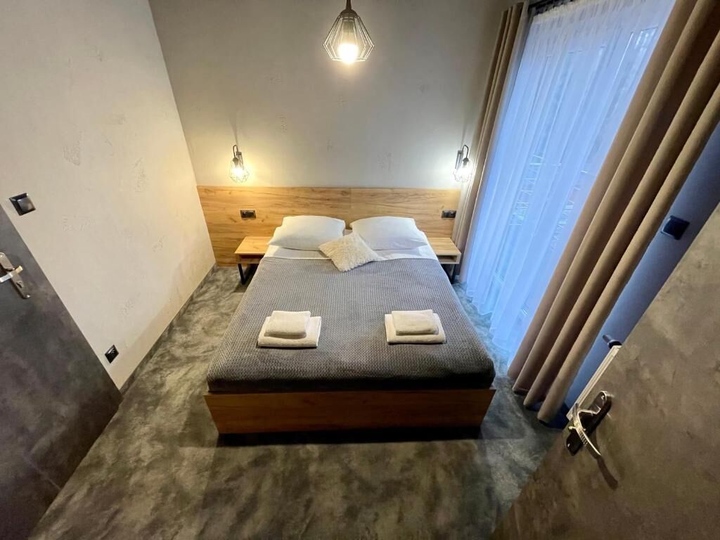 Une chambre à coucher comprenant un lit, deux tables de chevet, une tête de lit en bois et un luminaire suspendu.