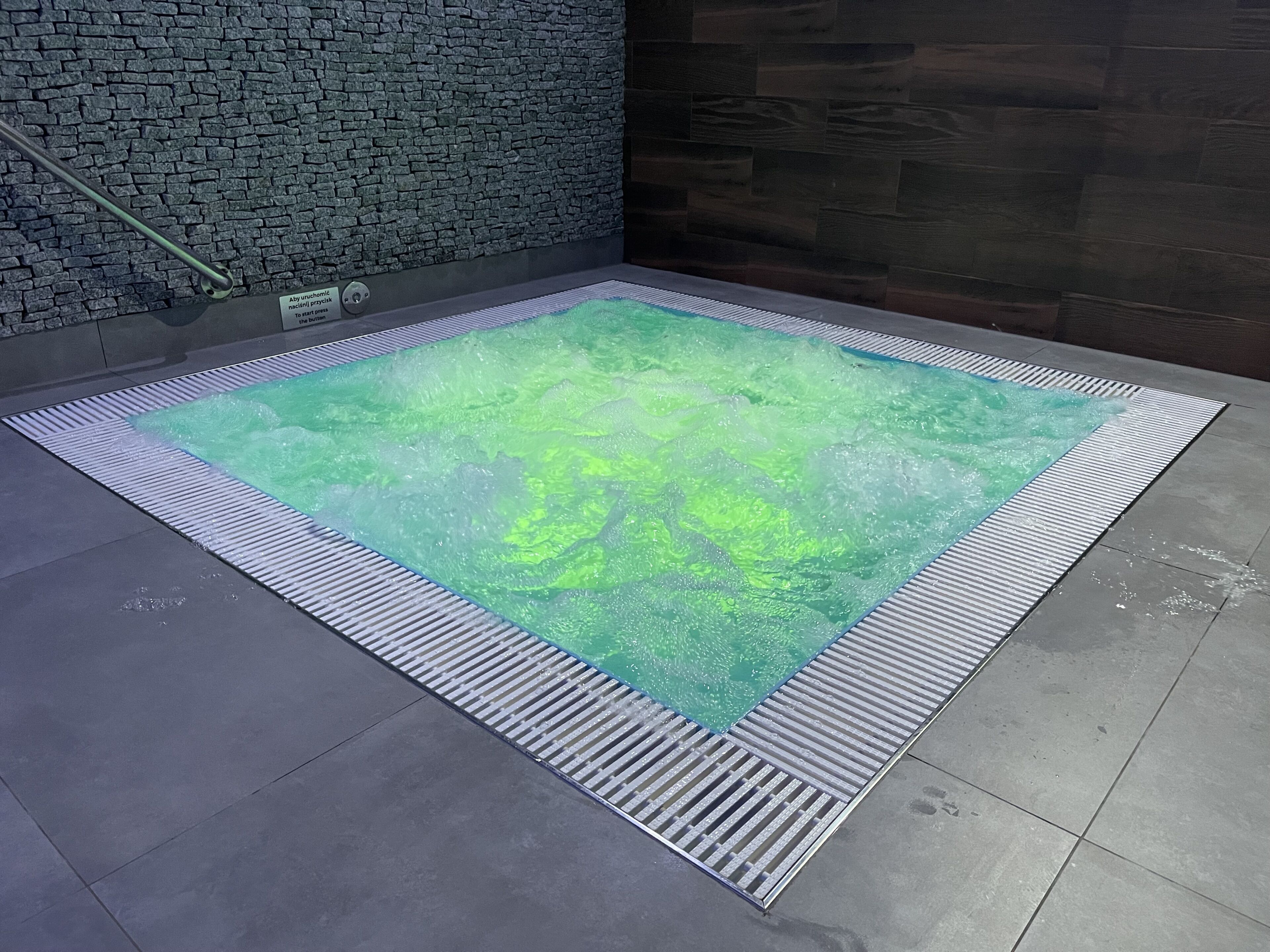 Un bain à remous rectangulaire, avec un mur à texture située derrière.