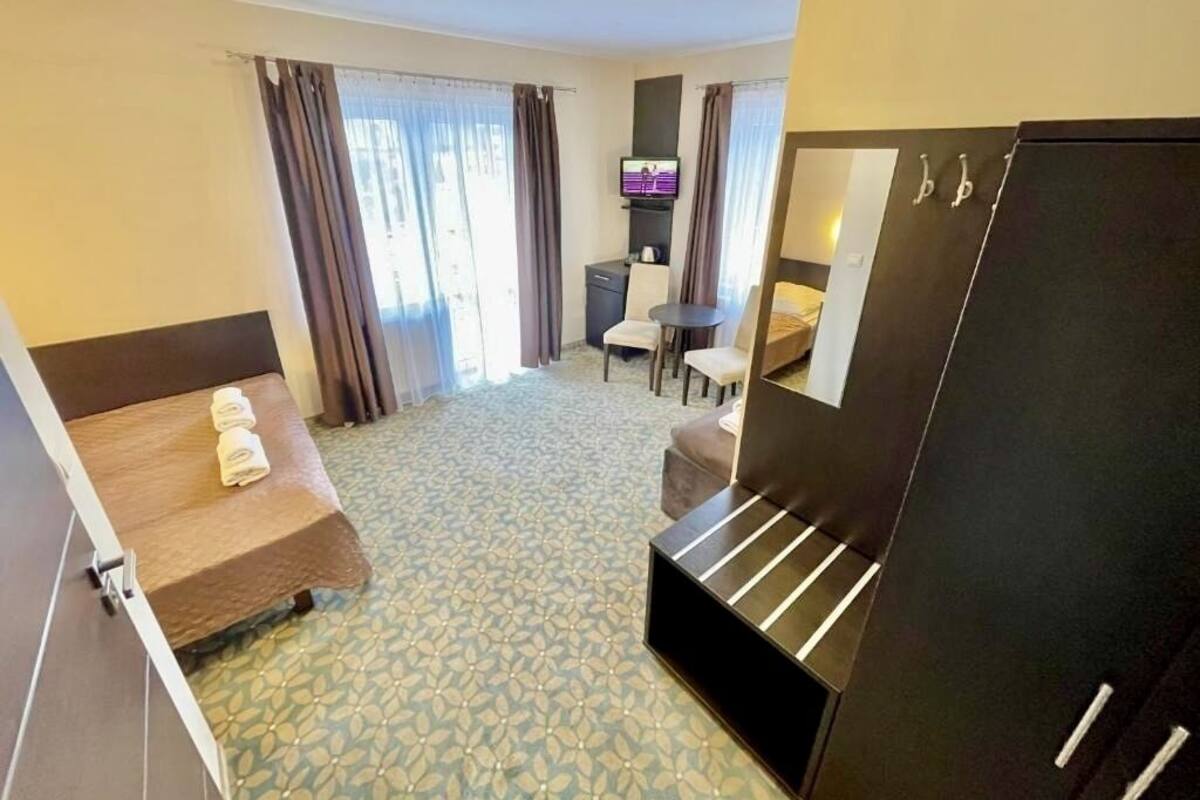 Quarto de hotel com cama, escrivaninha, cadeira, televisão e guarda-roupa.