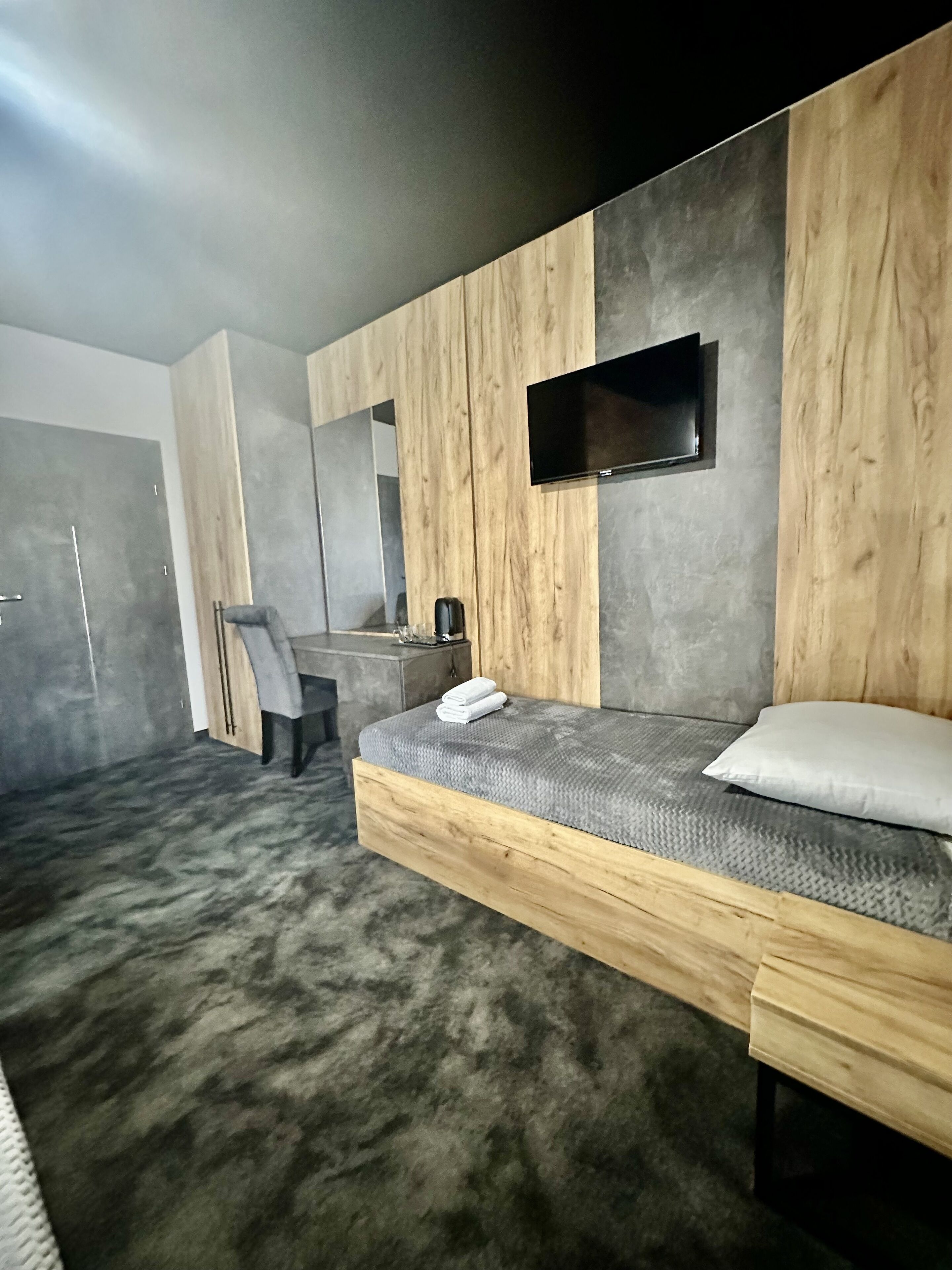 Un dormitorio moderno con una cama, una silla, un televisor y una mesita.