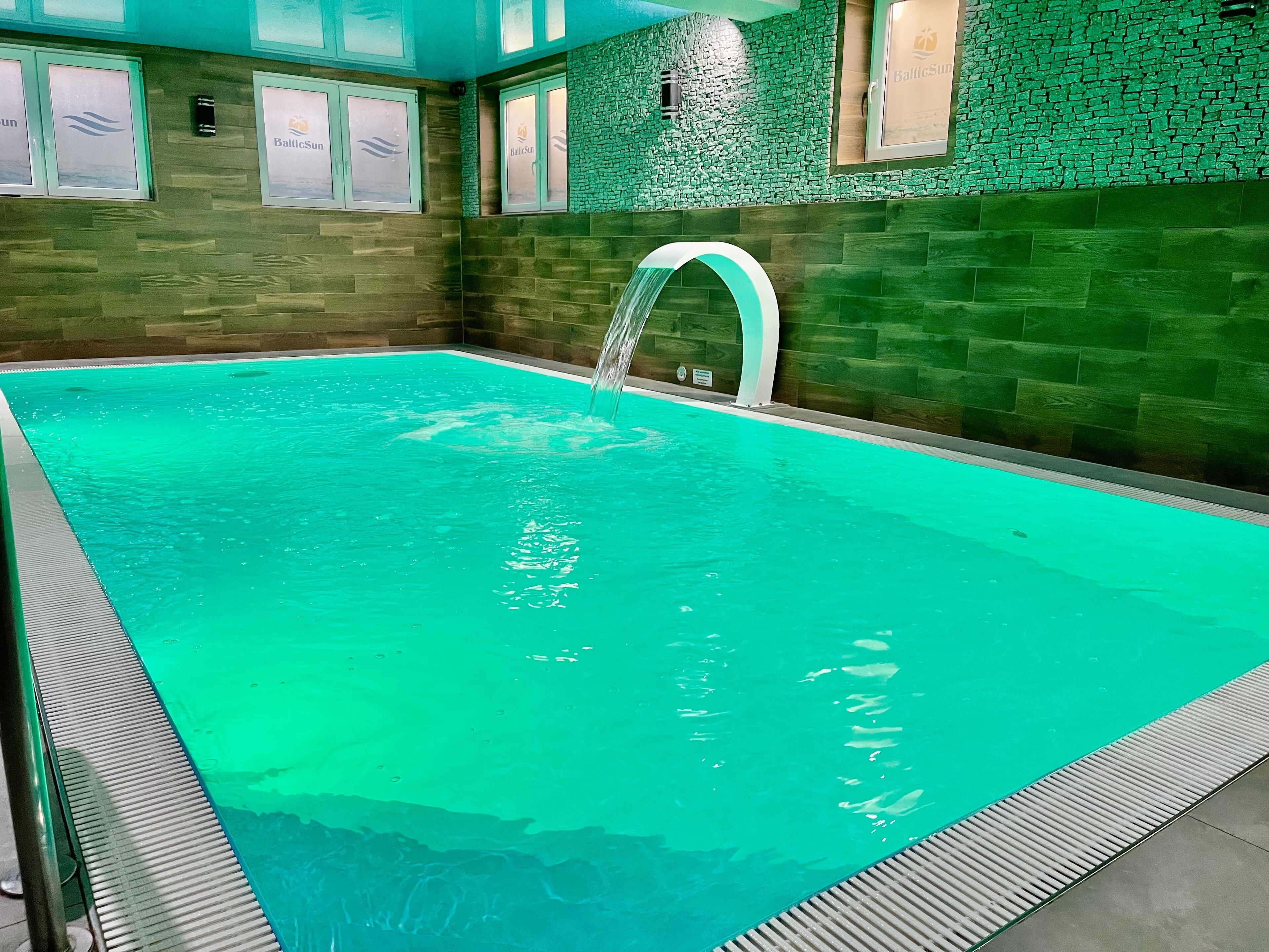 A swimming pool with a clear water feature, surrounded by a wooden wall with a green mosaic pattern.