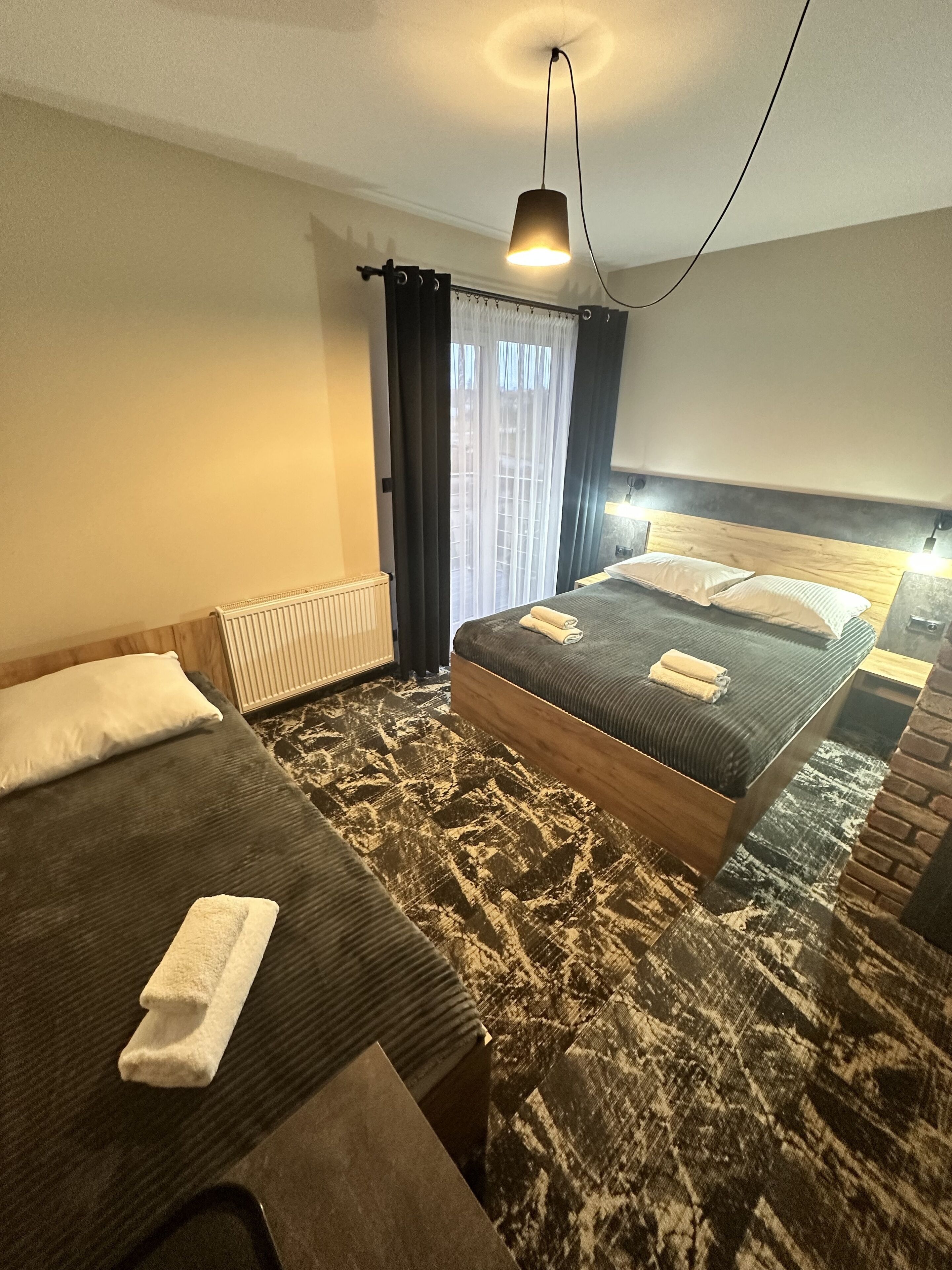 Une chambre d’hôtel avec deux lits, un radiateur, une moquette à motifs et un luminaire suspendu.