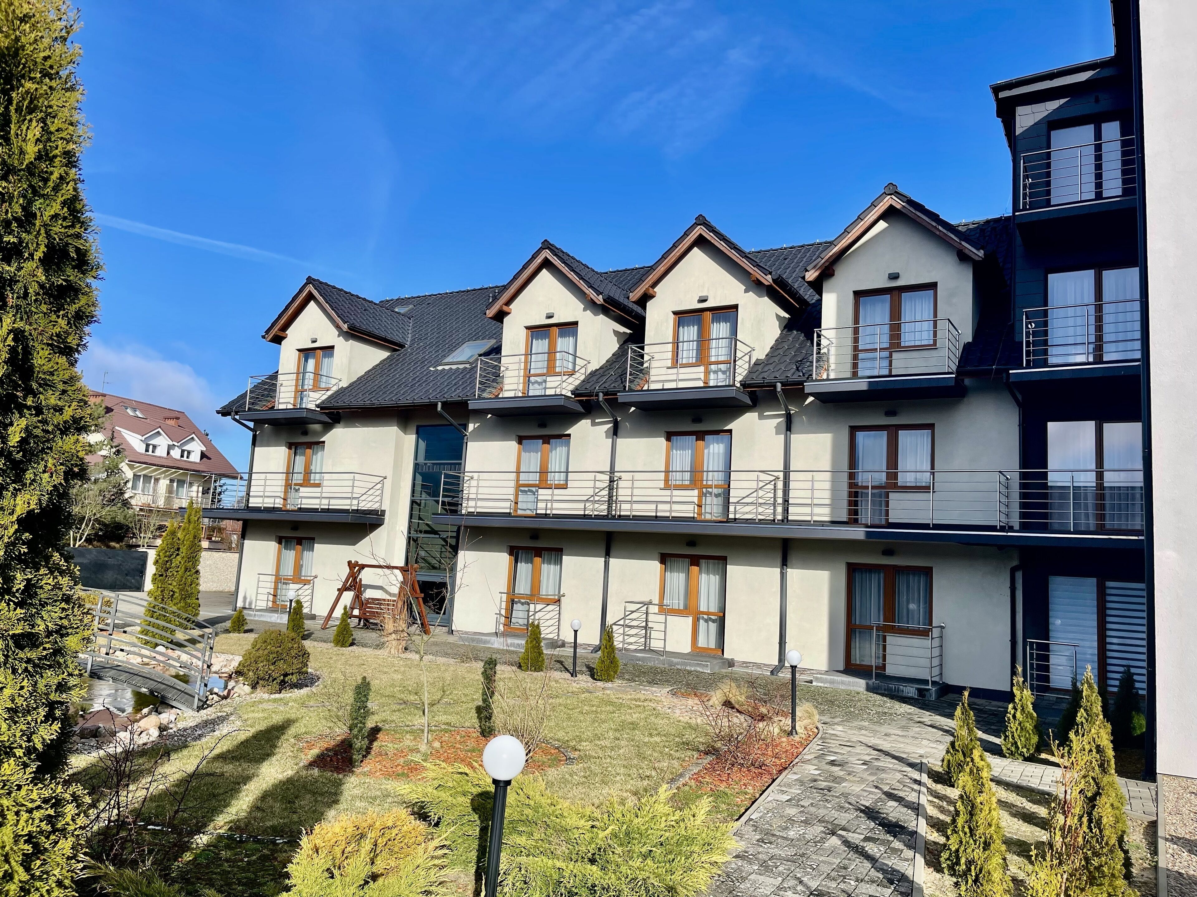 A multi-story residential building with balconies, a small garden area, and a bridge.