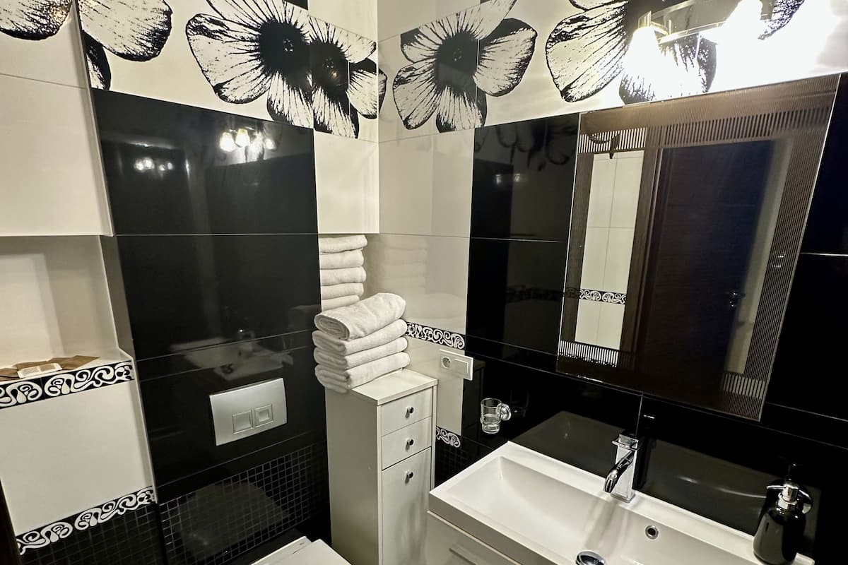 Casa de banho moderna com sanita, lavatório e espelho. Toalhas empilhadas na parede e um cesto de lixo.