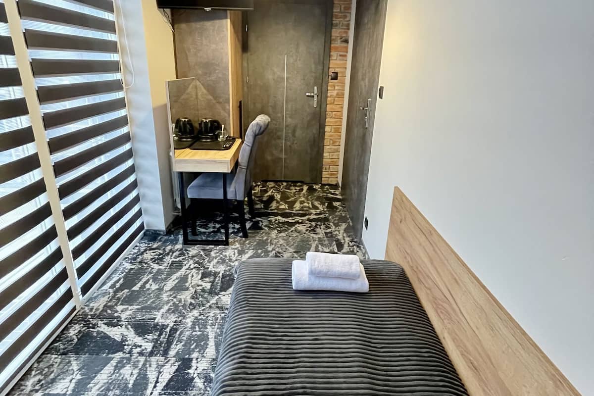 Quarto de hotel pequeno com cama, escrivaninha e chuveiro.