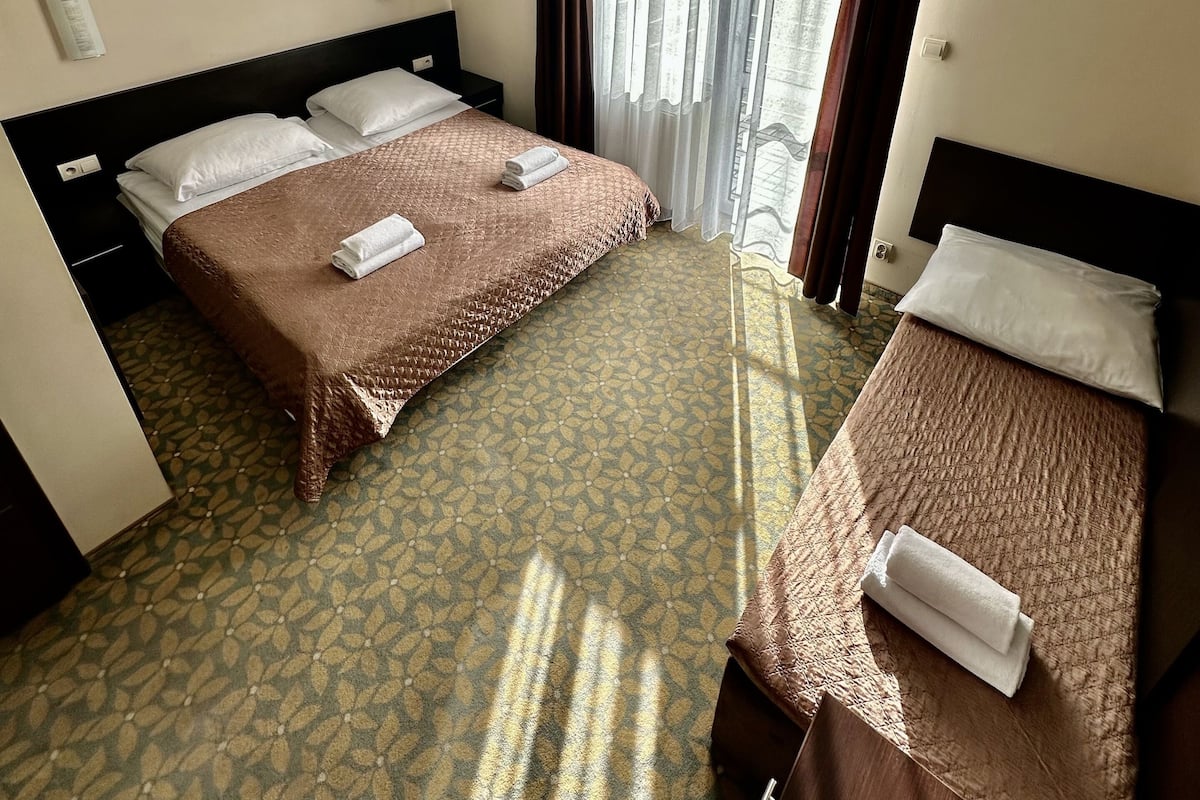 Quarto de hotel com duas camas, carpete estampado, janela com cortinas e luminária no teto.